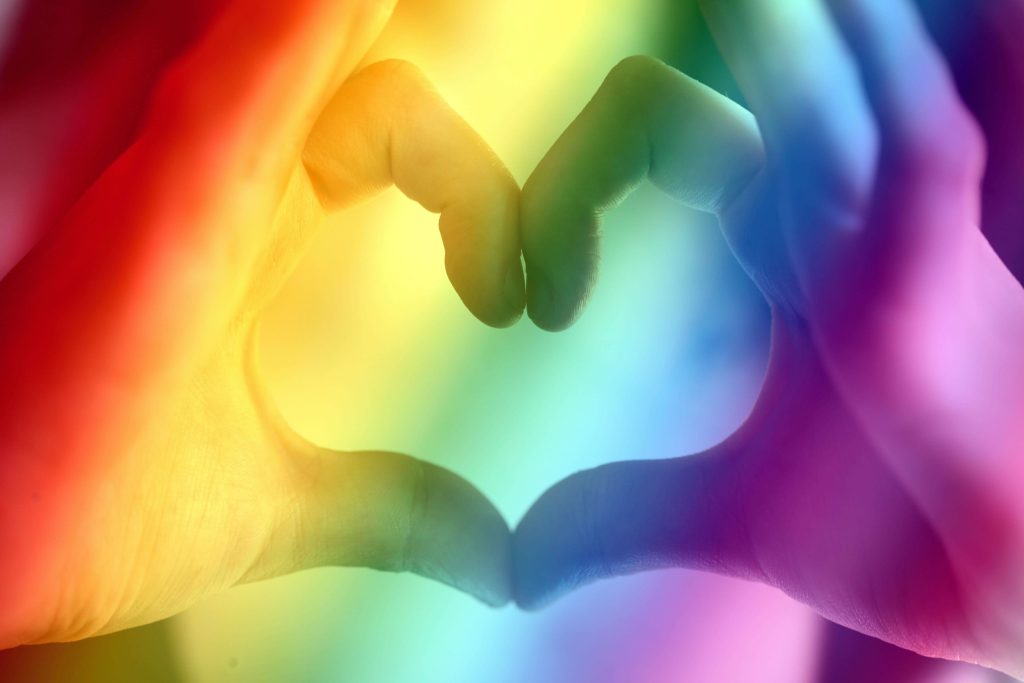 Imagen de referencia de la bandera LGBTIQ+ con el símbolo del corazón hecho con las manos. Foto Pexels